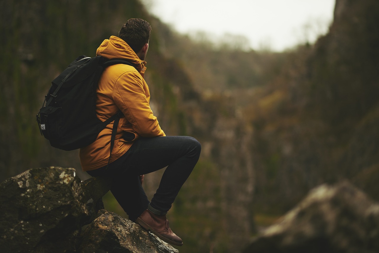 A man in a yellow jacket sitting on a mountain top admiring the views and meditating.