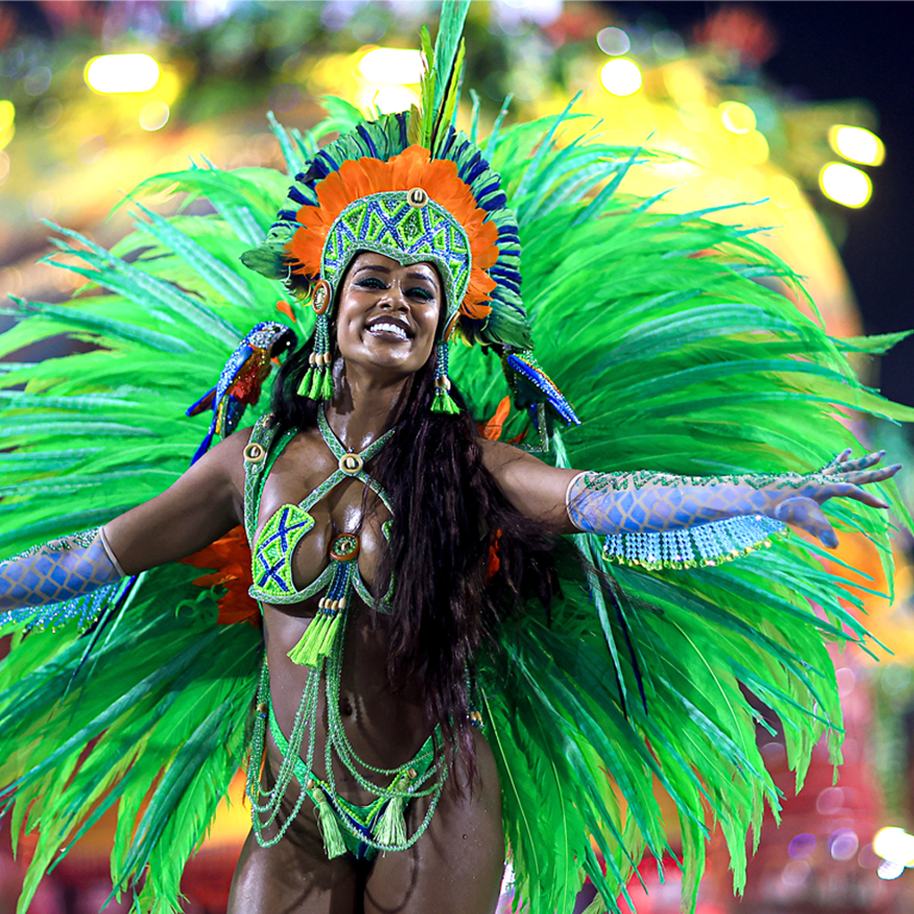 A woman from Brazil in a peacock-like flashing green costume with her arms wide open dancing at Carnival